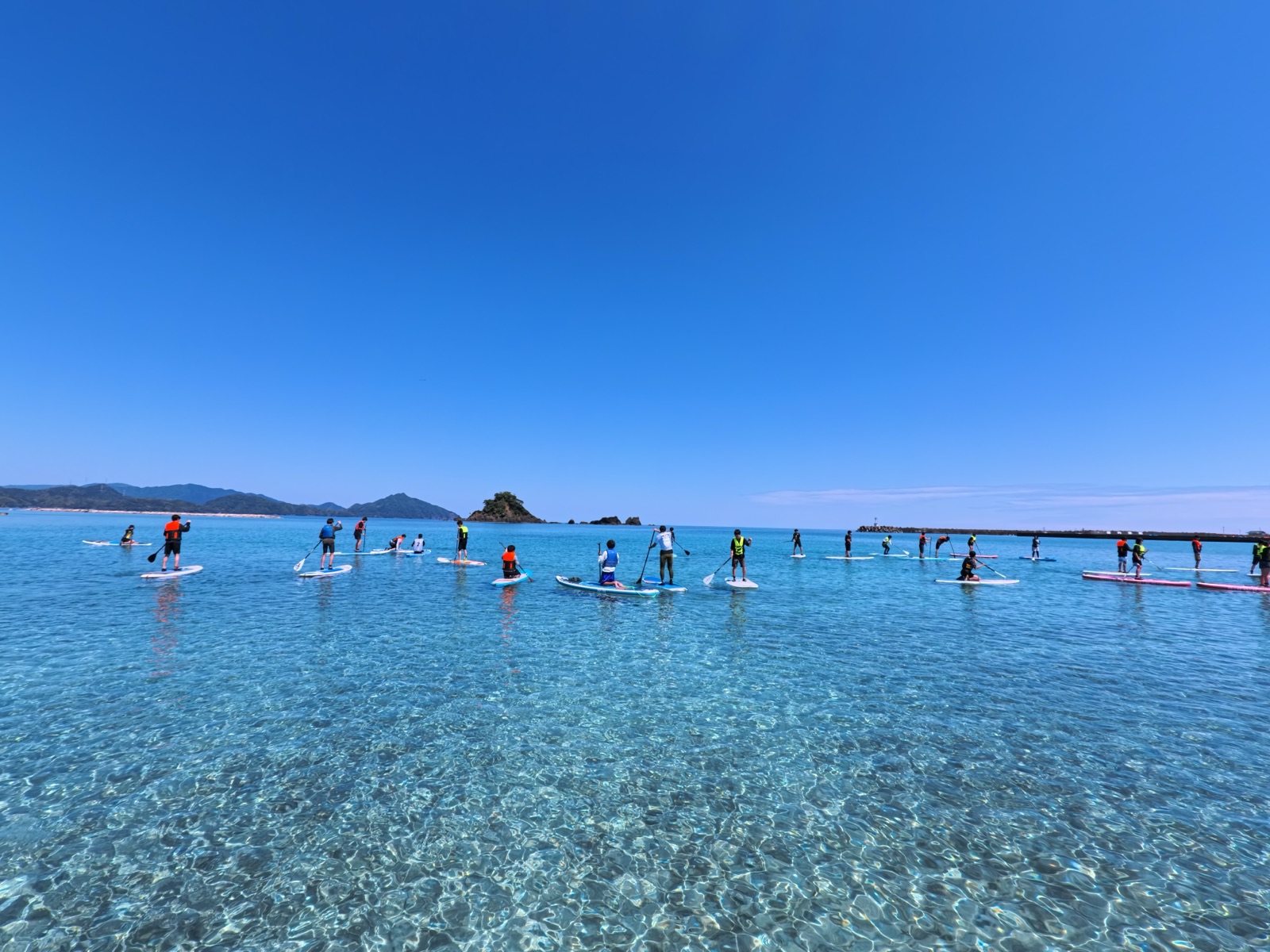 透明度の高い海でSUPをするグループ