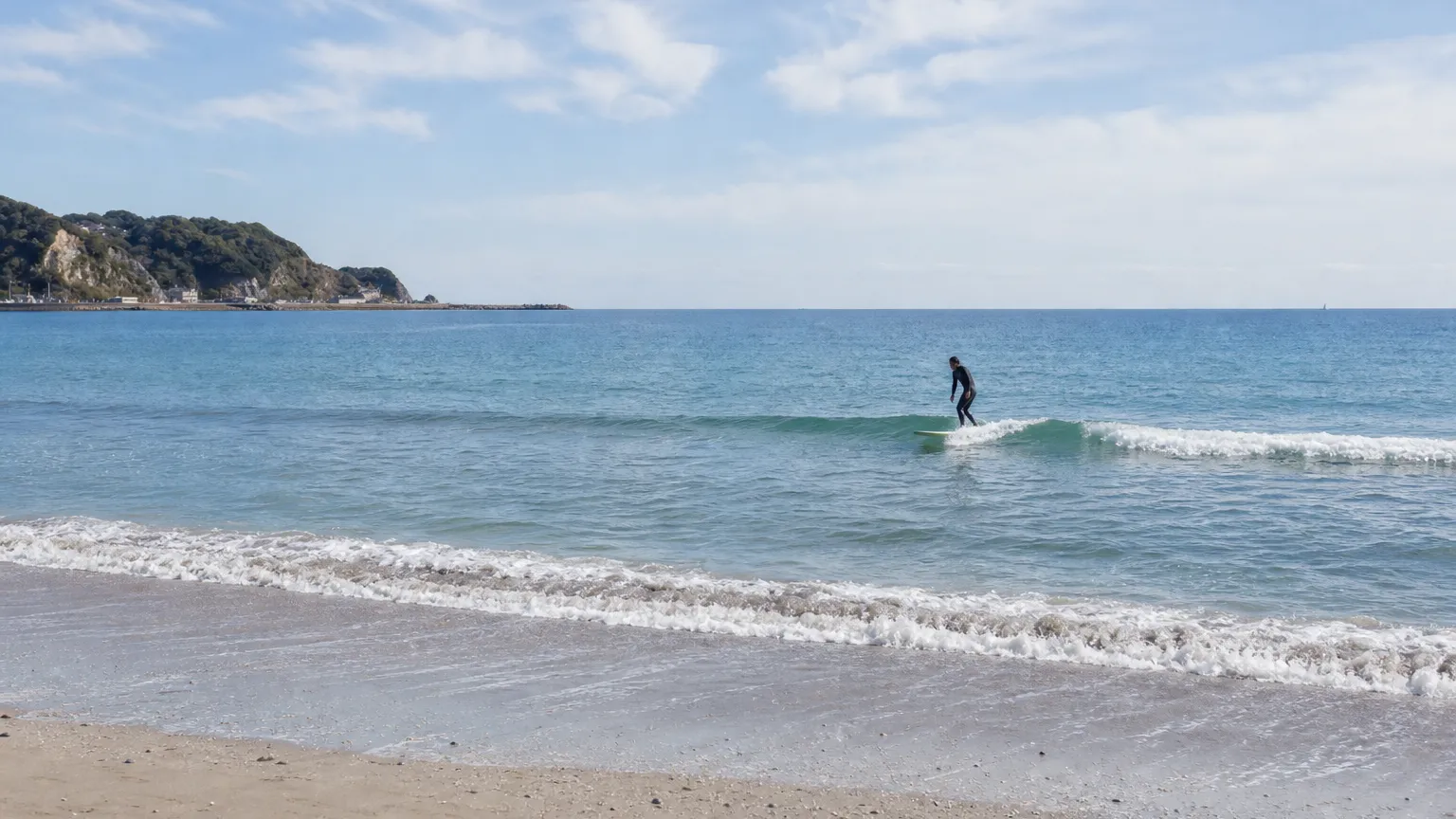 浜から見た、小さめの波に乗るサーファー(撮影イメージ)